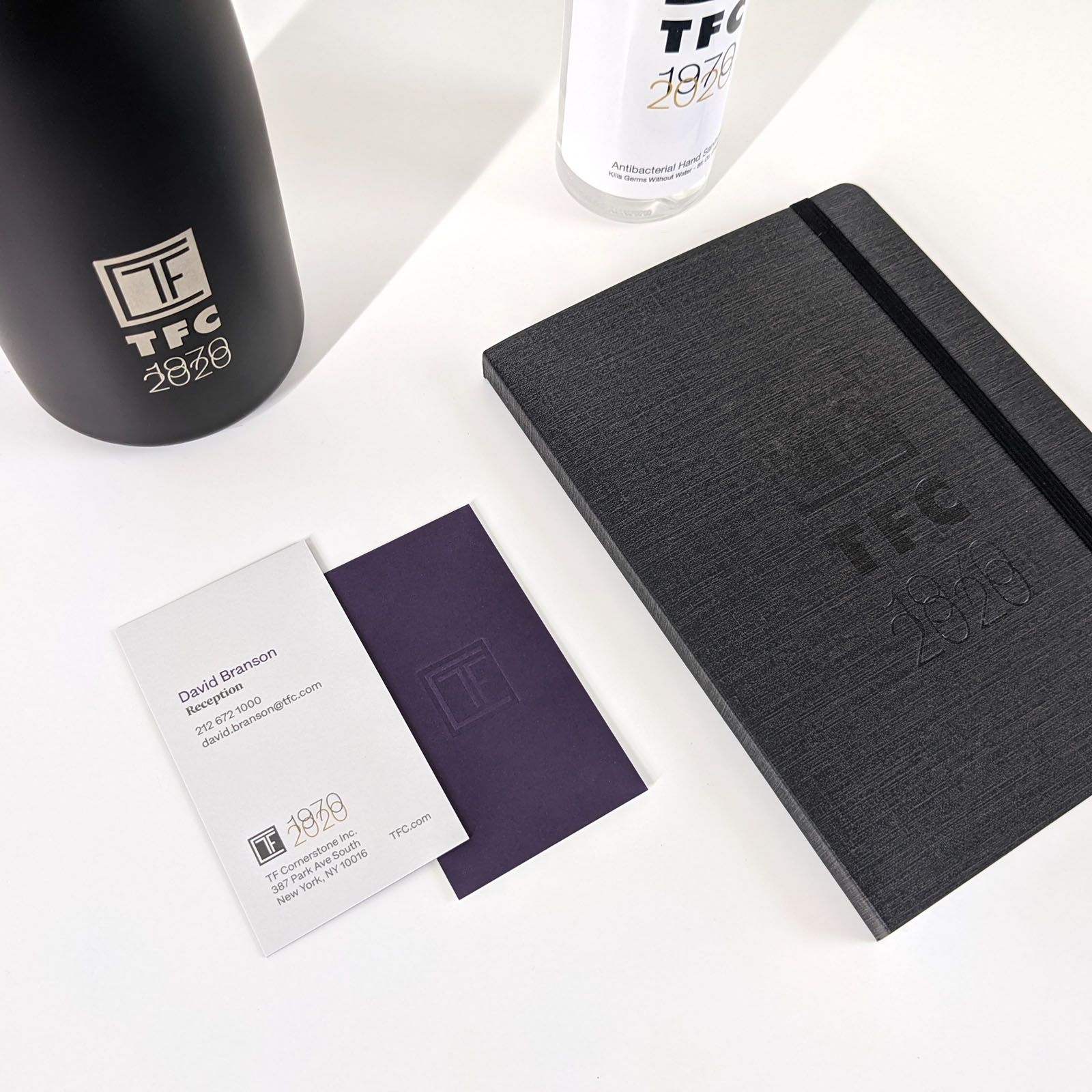 Photograph of a business card, small notebook, aluminum water bottle, and hand sanitizer. All items featuring the TFC 50th anniversary logo.