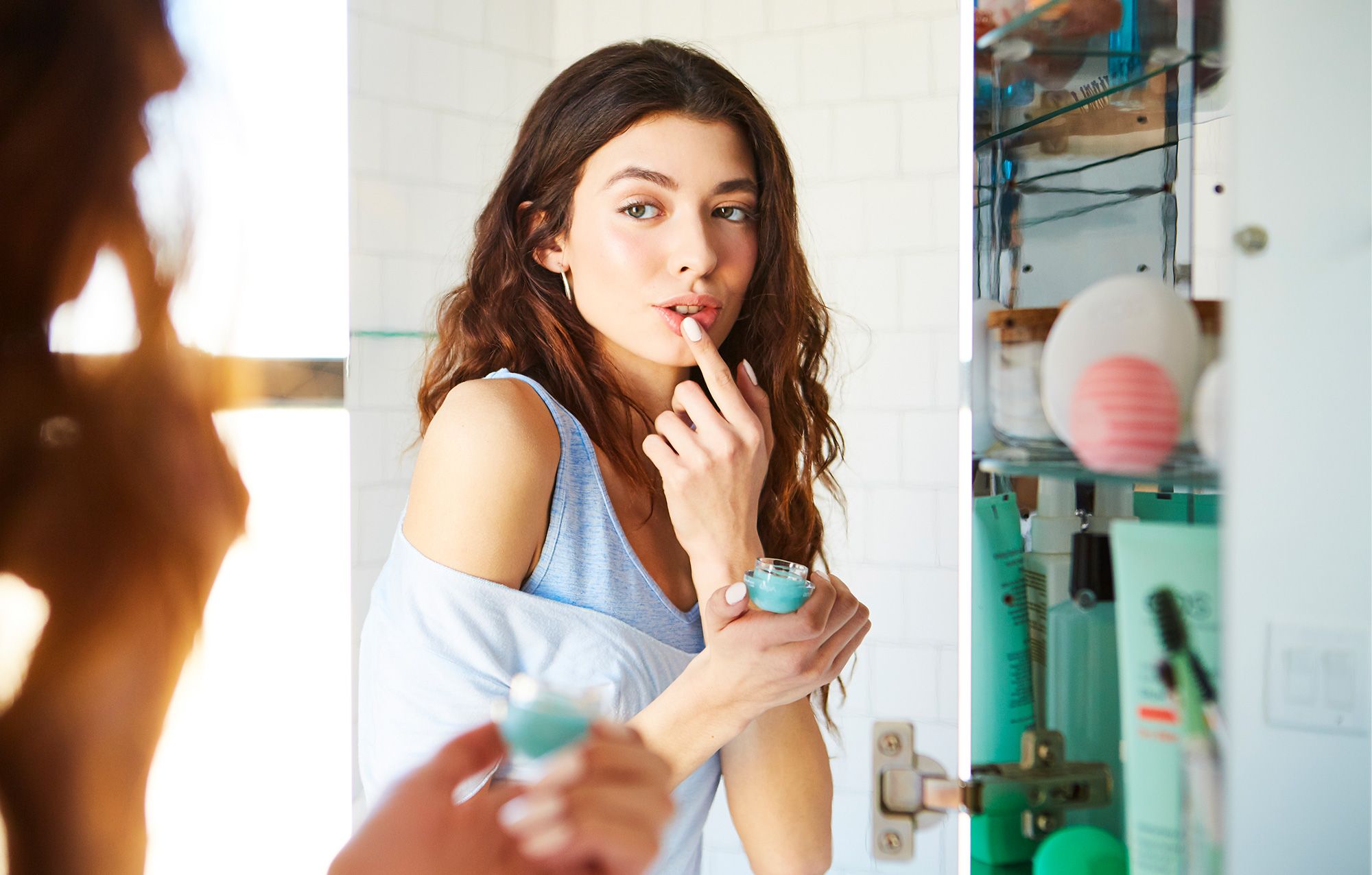 Photo of woman in a bathroom applying moisturizing lip balm with her finger